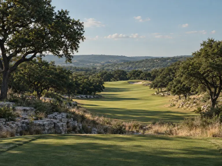 A Hill Country fairway winding between live oaks and limestone in morning light